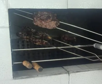 Churrasqueira de alvenaria da Pousada Casa da Barra com espetos de carne na brasa