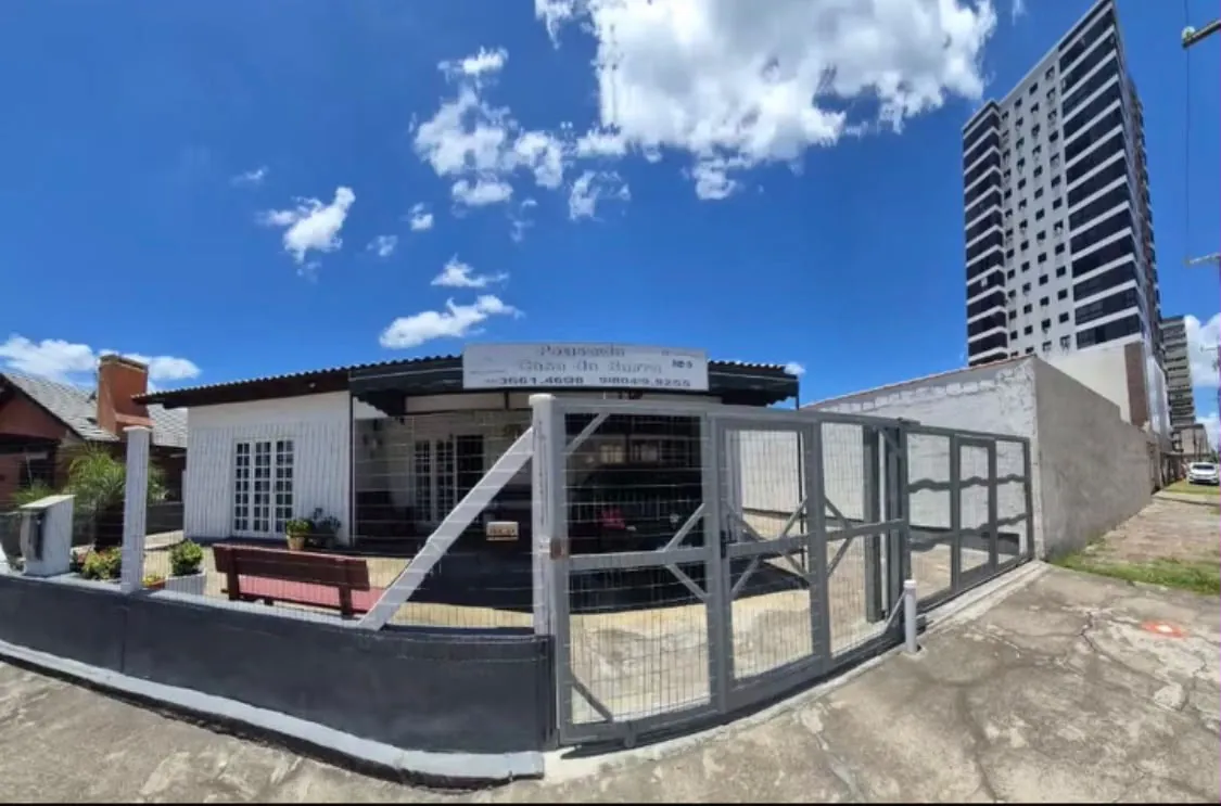 Fachada da Pousada Casa da Barra com portão fechado, varanda e placa com telefones, sob céu azul, na Rua 3 de Outubro, em Tramandaí